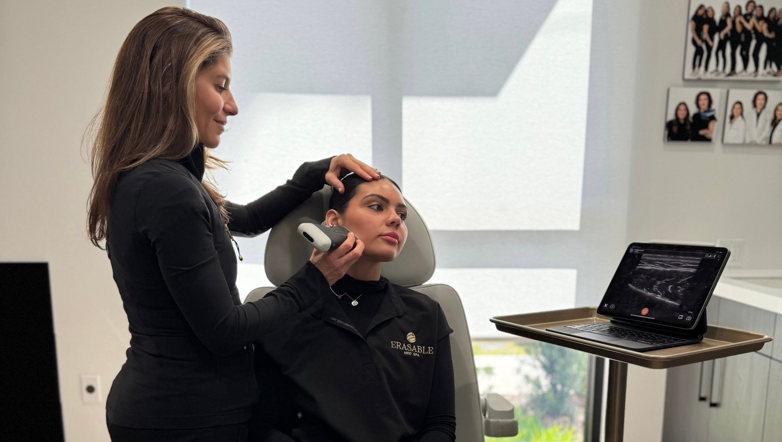 Laura Osterweil performing an ultrasound-guided facial consultation on a female patient, holding a probe near the jawline area.