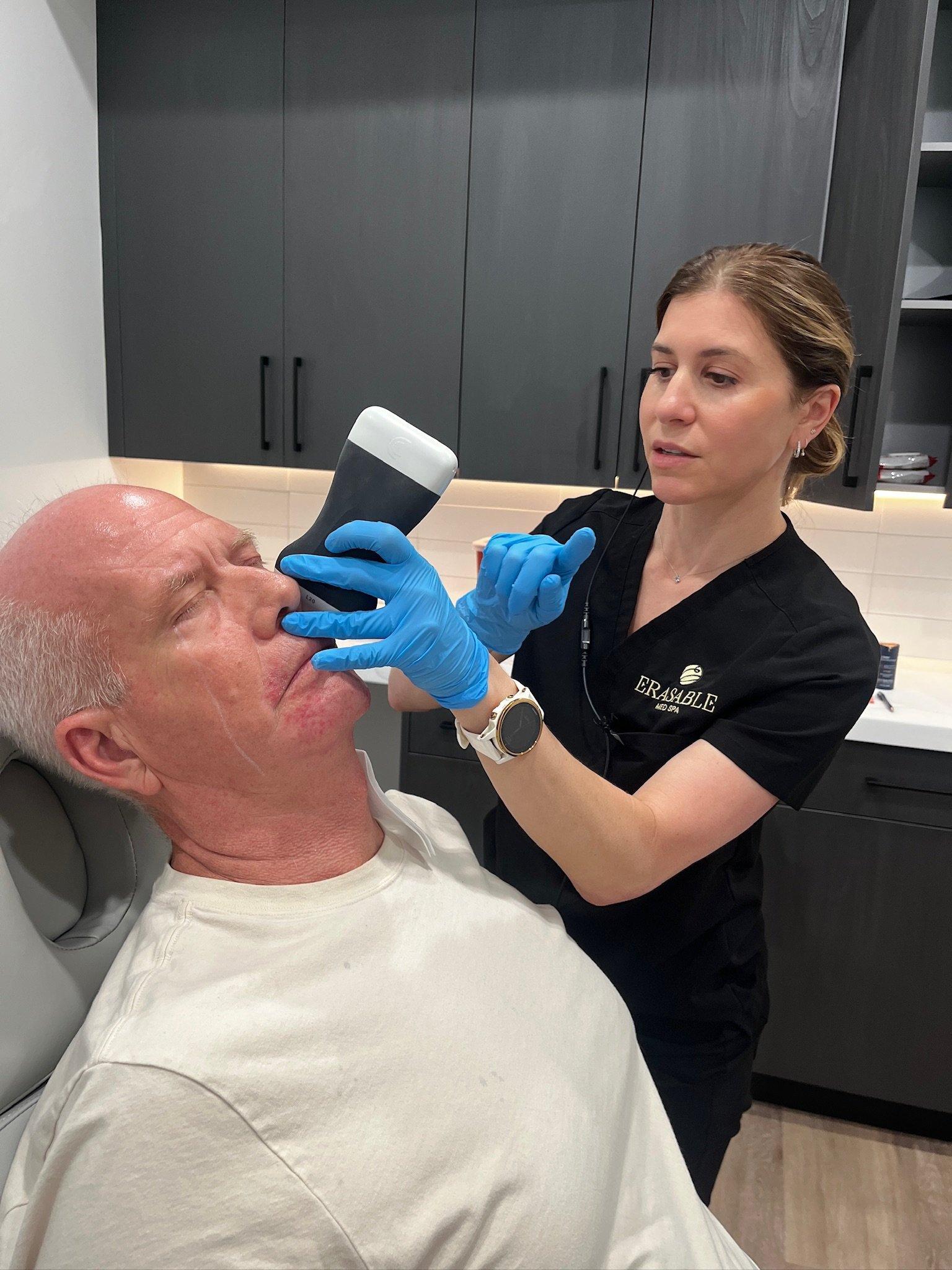 Laura Osterweil using ultrasound guidance for an injection on a male patient’s face in a clinical treatment room.